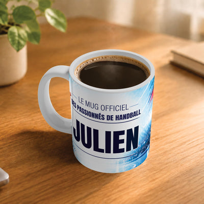 Café fumant dans le mug handball posé sur un bureau en bois : la phrase « Le mug officiel des passionnés de handball » et son prénom en grandes capitales, mug livré chez vous (exemple)