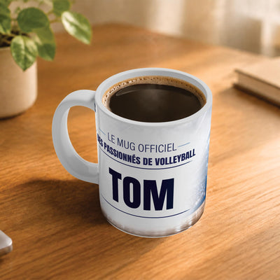 Exemple d'usage : le mug volleyball rempli de café sur une table en bois ; 330 ml de céramique blanche, votre prénom imprimé sous le titre, livré à domicile (exemple)
