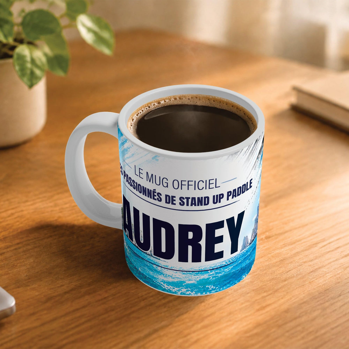 Exemple d'usage : le mug stand up paddle femme rempli de café sur une table en bois ; 330 ml de céramique blanche, votre prénom imprimé sous le titre, livré à domicile (exemple)
