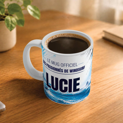 Exemple d'usage : le mug windsurf femme rempli de café sur une table en bois ; 330 ml de céramique blanche, votre prénom imprimé sous le titre, livré à domicile (exemple)