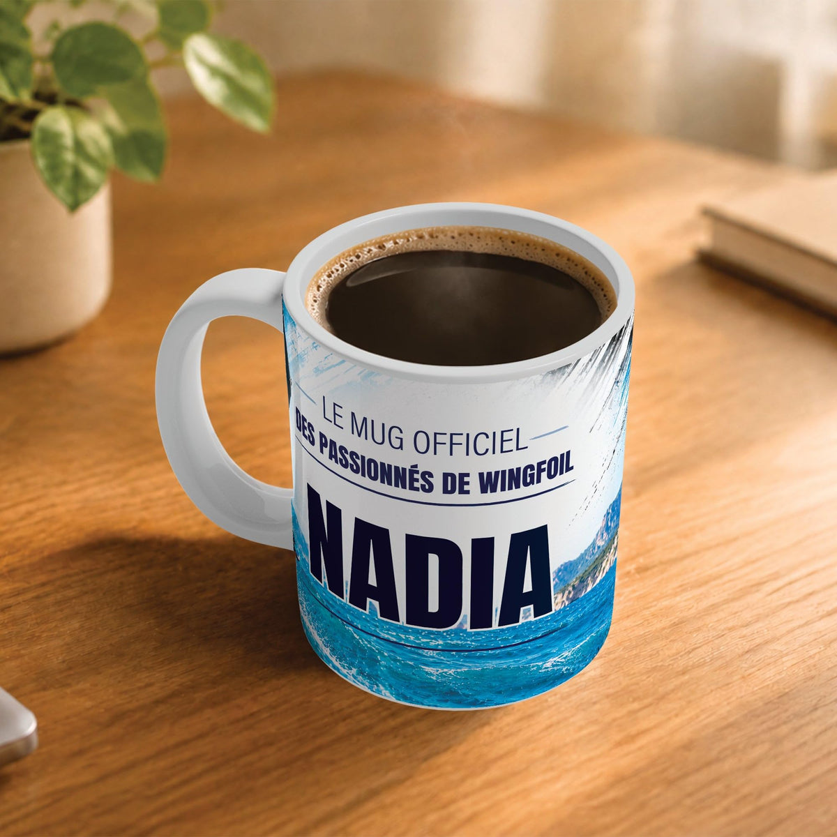Exemple d'usage : le mug wingfoil femme rempli de café sur une table en bois ; 330 ml de céramique blanche, votre prénom imprimé sous le titre, livré à domicile (exemple)