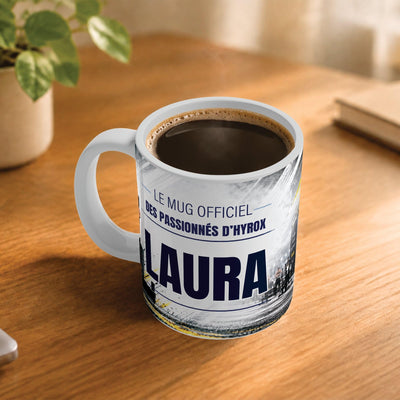 Café fumant dans le mug façon Hyrox posé sur un bureau en bois : la phrase « Le mug officiel » et son prénom en grandes capitales, mug livré chez vous (exemple)