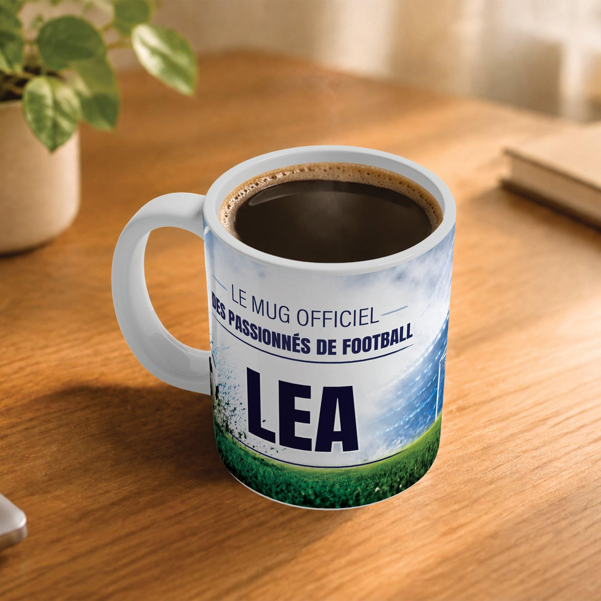 Café fumant dans le mug football posé sur un bureau en bois : la phrase « Le mug officiel des passionnés de football » et son prénom en grandes capitales, mug livré chez vous (exemple)