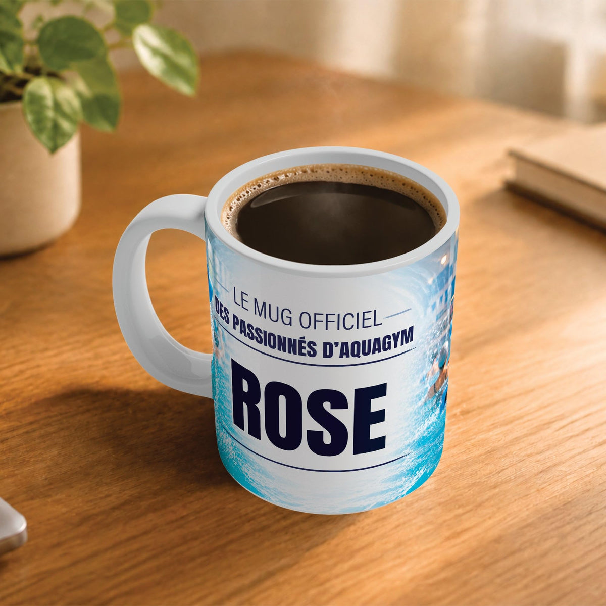 Café fumant dans le mug aquagym posé sur un bureau en bois : la phrase « Le mug officiel des passionnés d'aquagym » et son prénom en grandes capitales, mug livré chez vous (exemple)