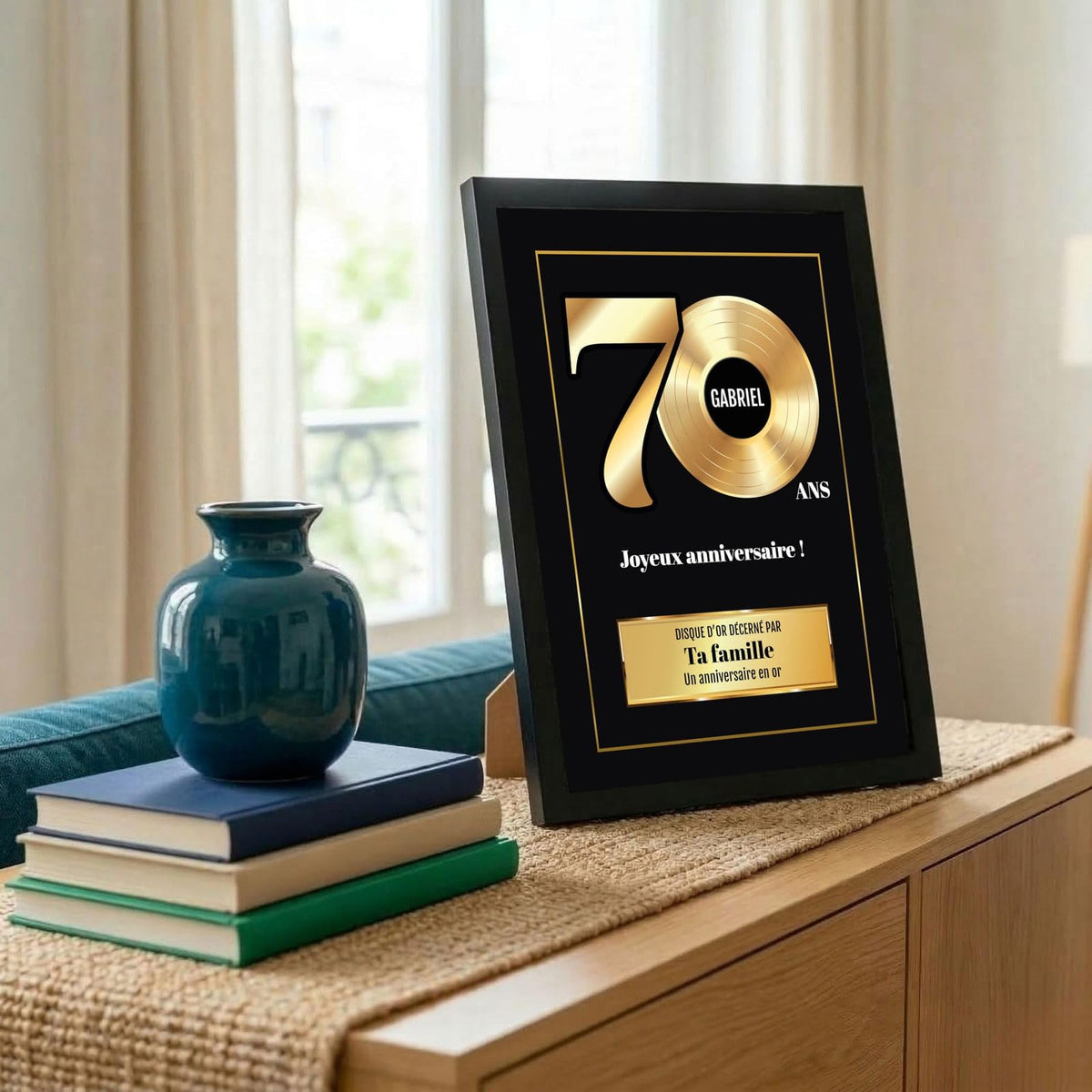 Disque d'or « 70 ans » en cadre noir posé sur un meuble : chiffres et disque dorés, prénom, signature et message personnalisés, livré chez vous (exemple)