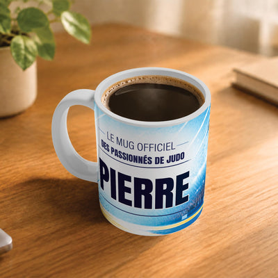 Café fumant dans le mug judo posé sur un bureau en bois : la phrase « Le mug officiel des passionnés de judo » et son prénom en grandes capitales, mug livré chez vous (exemple)