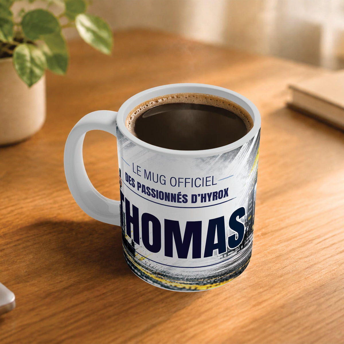 Café fumant dans le mug façon Hyrox posé sur un bureau en bois : la phrase « Le mug officiel » et son prénom en grandes capitales, mug livré chez vous (exemple)