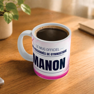 Café fumant dans le mug gymnastique posé sur un bureau en bois : la phrase « Le mug officiel des passionnés de gymnastique » et son prénom en grandes capitales, mug livré chez vous (exemple)
