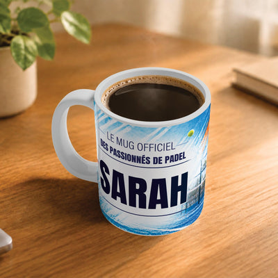 Exemple d'usage : le mug padel femme rempli de café sur une table en bois ; 330 ml de céramique blanche, votre prénom imprimé sous le titre, livré à domicile (exemple)