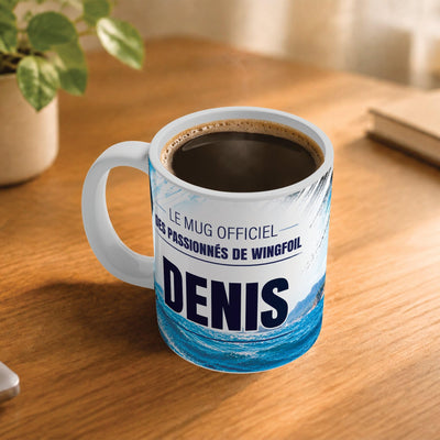 Exemple d'usage : le mug wingfoil rempli de café sur une table en bois ; 330 ml de céramique blanche, votre prénom imprimé sous le titre, livré à domicile (exemple)