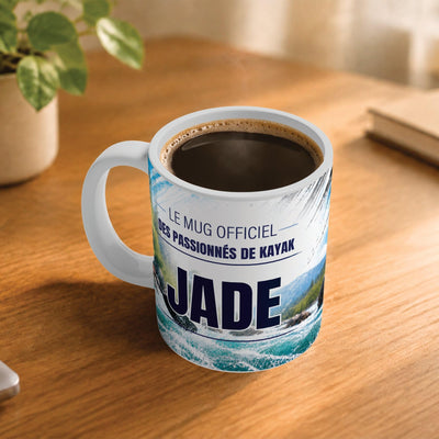 Café fumant dans le mug kayak posé sur un bureau en bois : la phrase « Le mug officiel des passionnés de kayak » et son prénom en grandes capitales, mug livré chez vous (exemple)