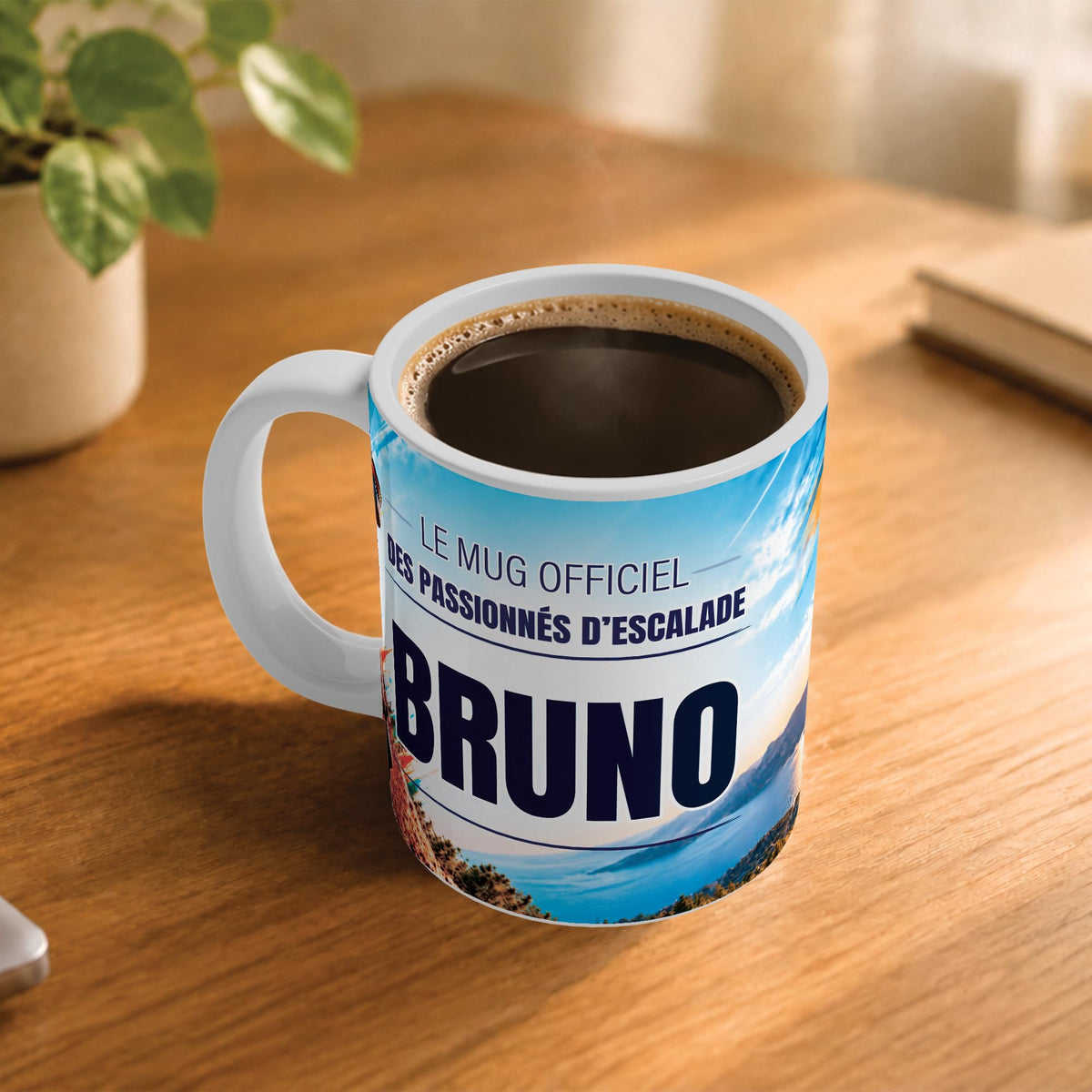 Café fumant dans le mug escalade posé sur un bureau en bois : la phrase « Le mug officiel des passionnés d'escalade » et son prénom en grandes capitales, mug livré chez vous (exemple)