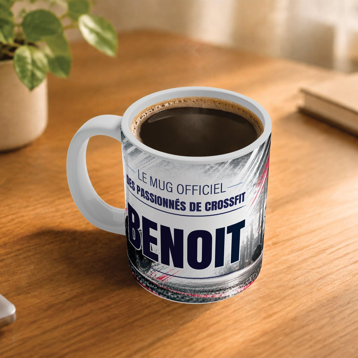 Café fumant dans le mug façon CrossFit posé sur un bureau en bois : la phrase « Le mug officiel » et son prénom en grandes capitales, mug livré chez vous (exemple)