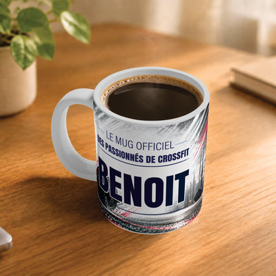 Café fumant dans le mug façon CrossFit posé sur un bureau en bois : la phrase « Le mug officiel » et son prénom en grandes capitales, mug livré chez vous (exemple)