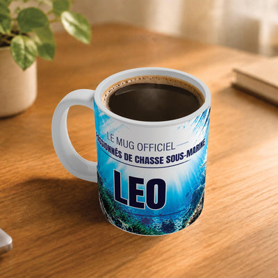 Café fumant dans le mug chasse sous-marine posé sur un bureau en bois : la phrase « Le mug officiel des passionnés de chasse sous-marine » et son prénom en capitales, mug livré chez vous (exemple)