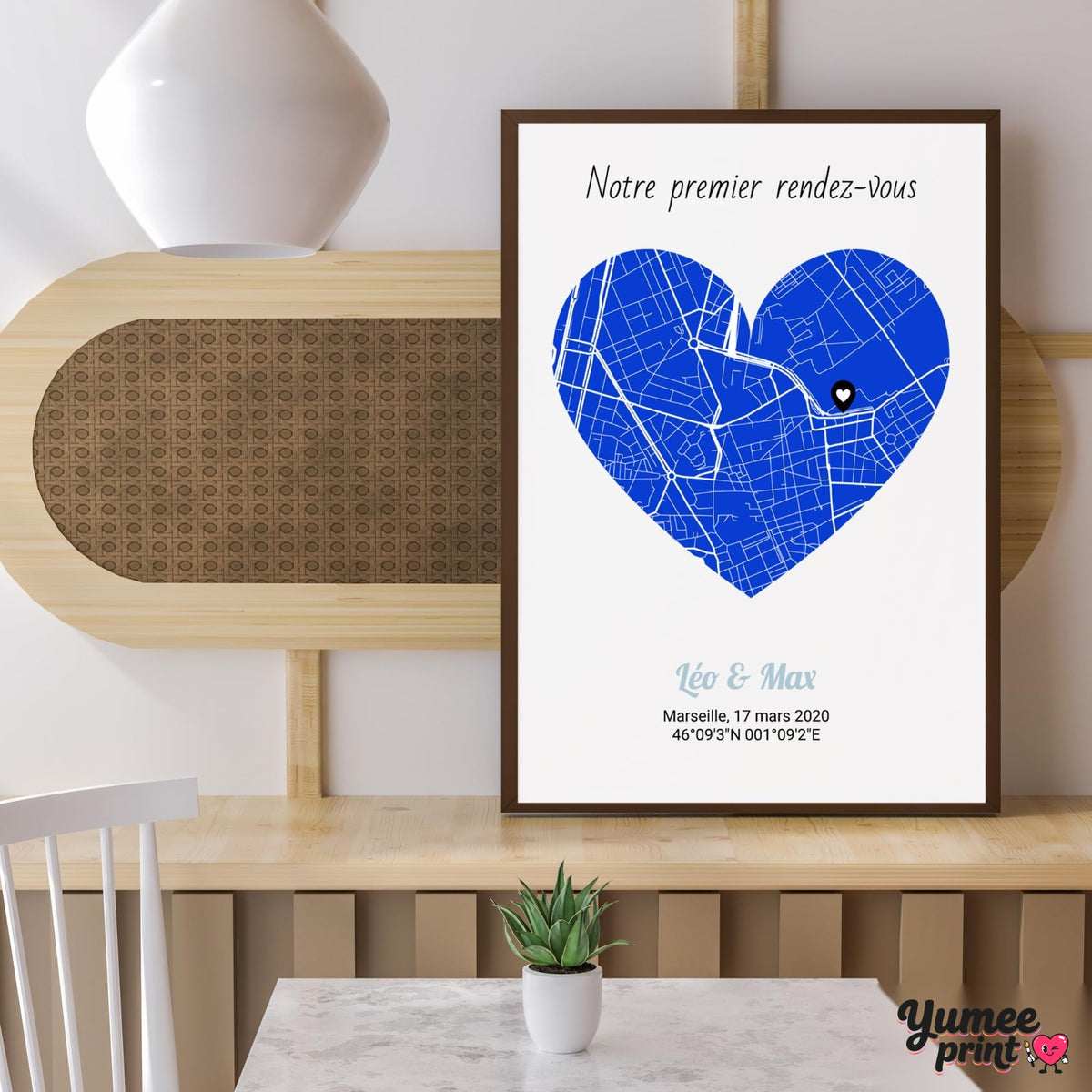 Carte en cœur teinte bleue sur fond blanc, en cadre bois foncé posé sur un meuble ; phrase, prénoms, date et coordonnées GPS de votre lieu, imprimés puis livrés chez vous (exemple)